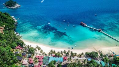 Aerial view of a tropical beach in Malaysia with clear waters, boats, and a pier